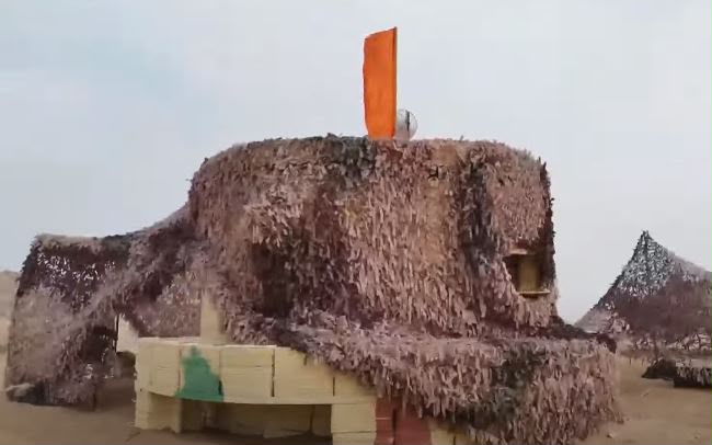 Camouflaged 3D-printed bunker in desert terrain.